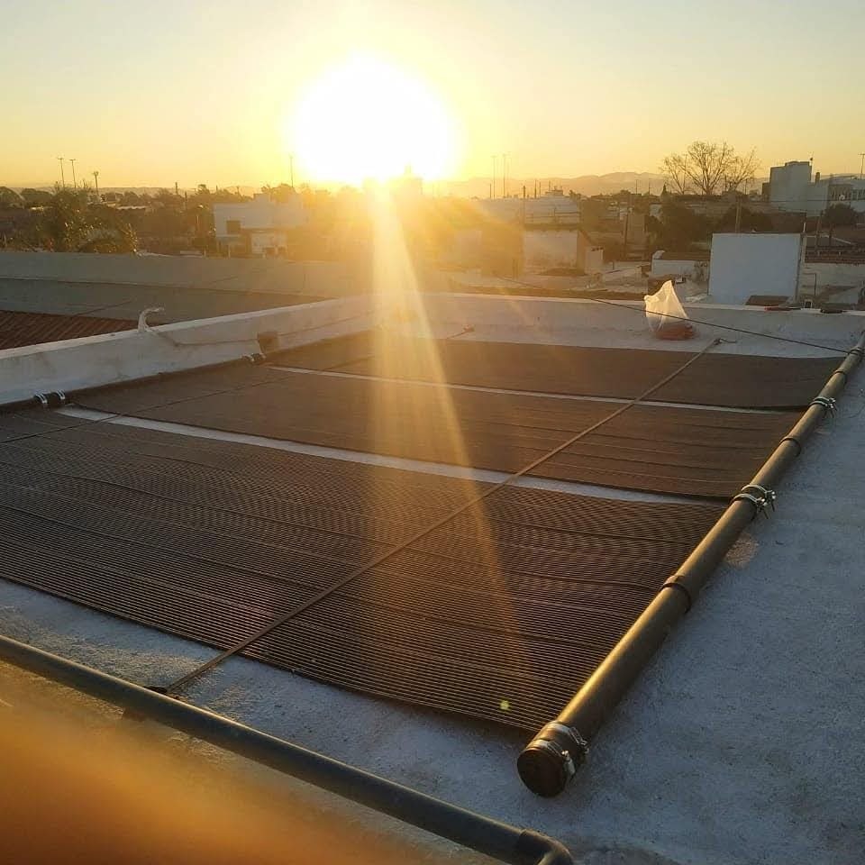 Captadores solares para climatización de piscina sobre cubierta, iluminados por el sol al atardecer.
